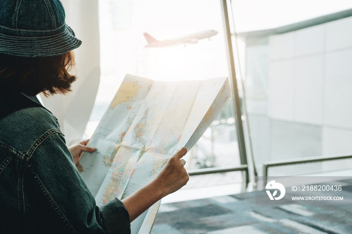 Young joyful traveler tourist woman with paper map, wait in lobby hall at airport. Passenger traveling abroad on weekend getaway. Air flight concept