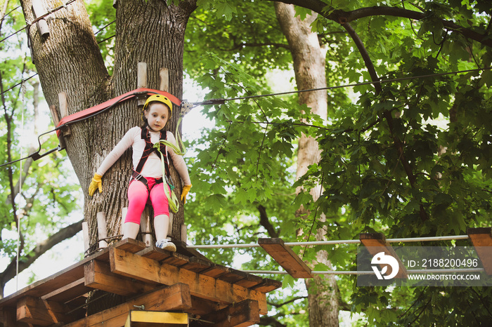 Girl climbing on a rope playground outdoor. Rope way - little girl is looking at the rope slideway fearing. Looking away with fear of extreme rope slide.