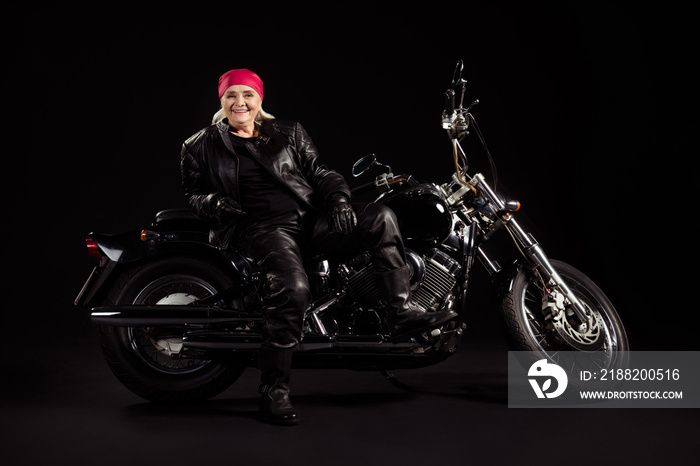 Full length photo of positive cool old woman biker sit motor bike enjoy motion freedom adventure wear modern clothes isolated over black color background