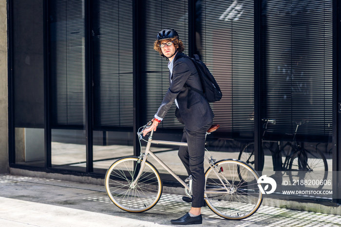 Portrait of hipster handsome businessman in suit with backpack looking forward while commuting riding bicycle on the street city way go to work.business travel transport bike concept