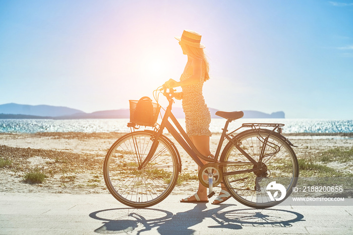 Carefree woman with bike riding on sand beach having fun, on the seaside promenade on a summer day.