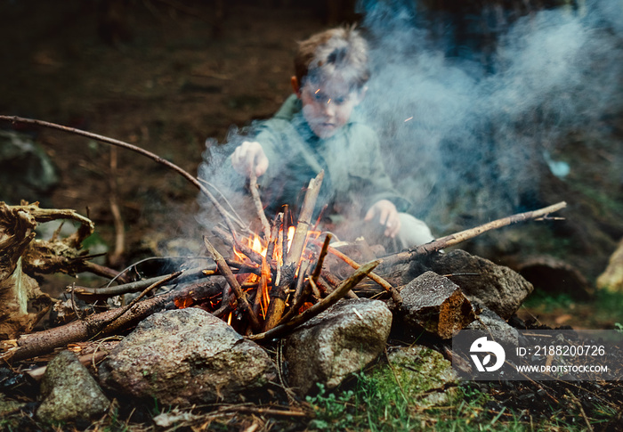 Little boy sits near campfire