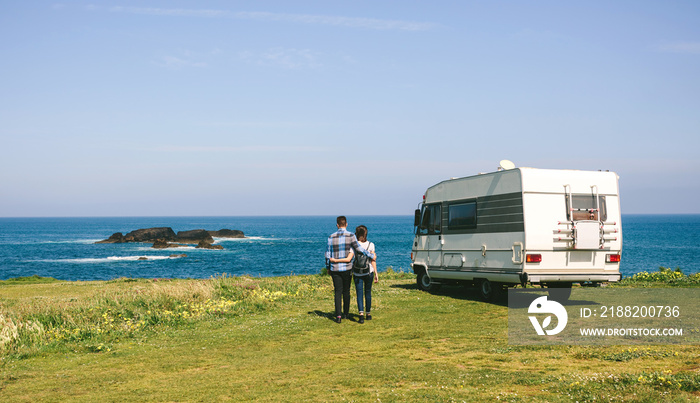 Young couple taking a walk near the coast with a camper in the background