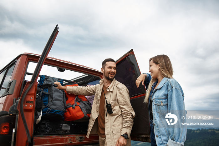 Cheerful young couple travelling while getting their backpacks from the trunk of their car