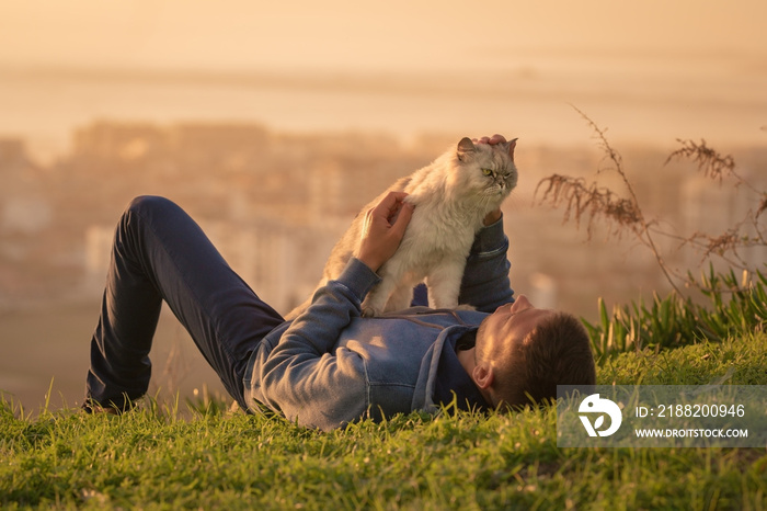 Man with his cat lying on the grass and enjoying life. Walking the cat. People and pets. Human and animal. Human and pet love concept. Cat with owner