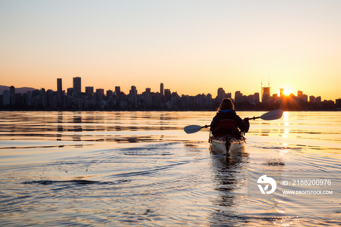 Adventurous girl on a sea kayak is kayaking during a vibrant sunny sunrise. Taken in Downtown Vancouver, British Columbia, Canada.