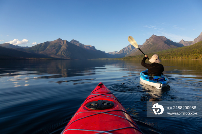 Adventurous Man Kayaking in Lake McDonald during a sunny summer evening with American Rocky Mountains in the background. Taken in Glacier National Park, Montana, USA.