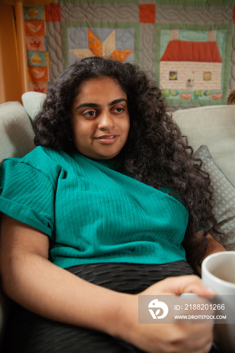 Curvy Indian girl with Cerebral Palsy drinking coffee next to her dog in the living room