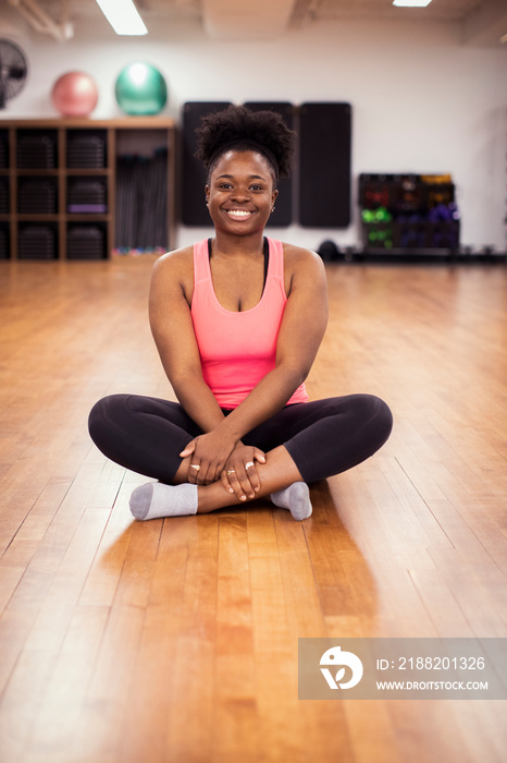 Portrait of smiling female athlete sitting on hardwood floor in gym