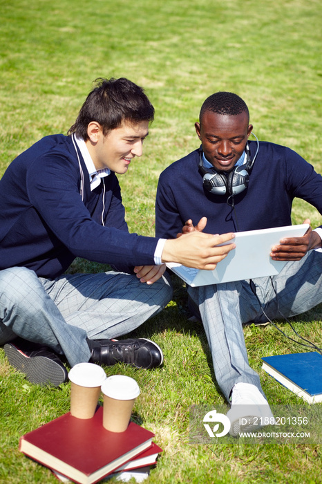 Two students sitting outdoors and using laptop