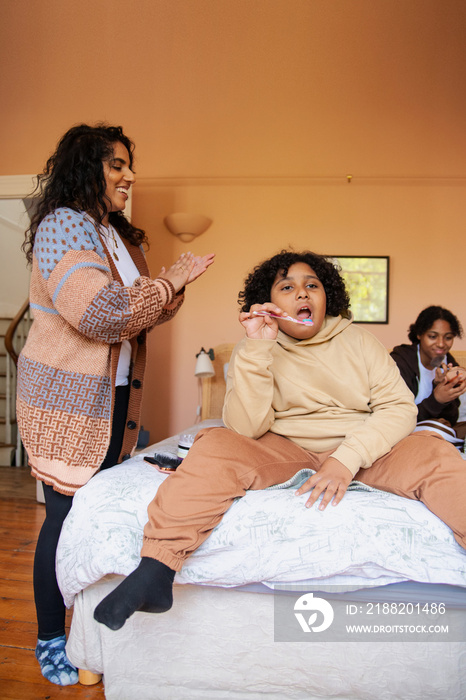 Mid-sized mother helping her son with his hair while he brushes his teeth