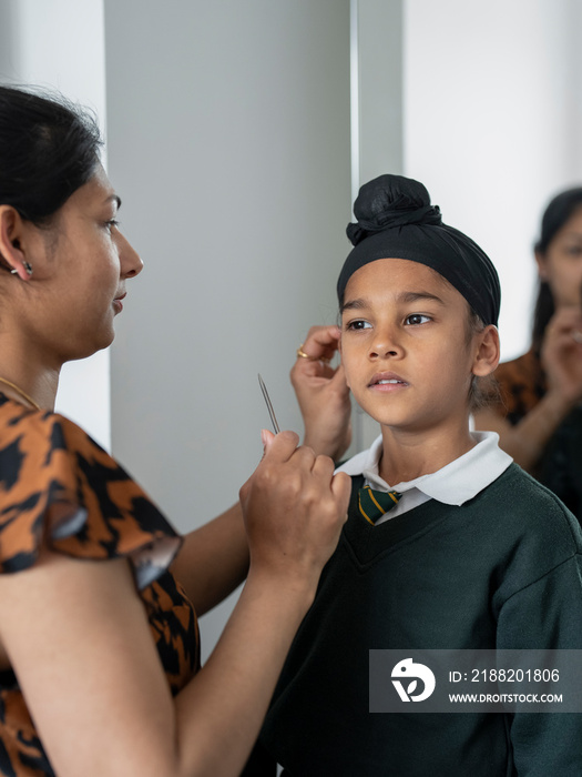 Mother wrapping traditional turban on son’s (6-7) head