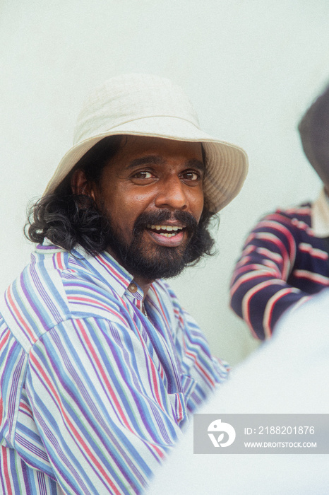 Malaysian Indian men in a group against a cloth backdrop in a park surrounded by trees, talking, laughing and sitting together