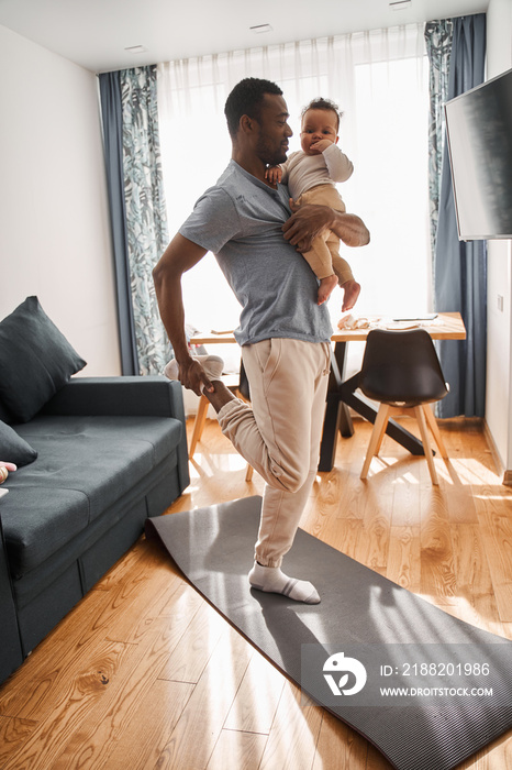 Multiracial man holding his son at the hands while meditating and practicing yoga