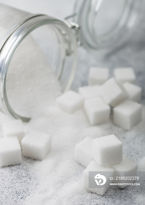 Glass jar of natural white refined sugar with cubes on light table background.