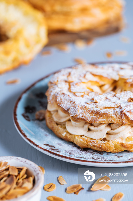 Dessert called Paris Brest on a grey background with powder sugar and almond leaves and almond creme between