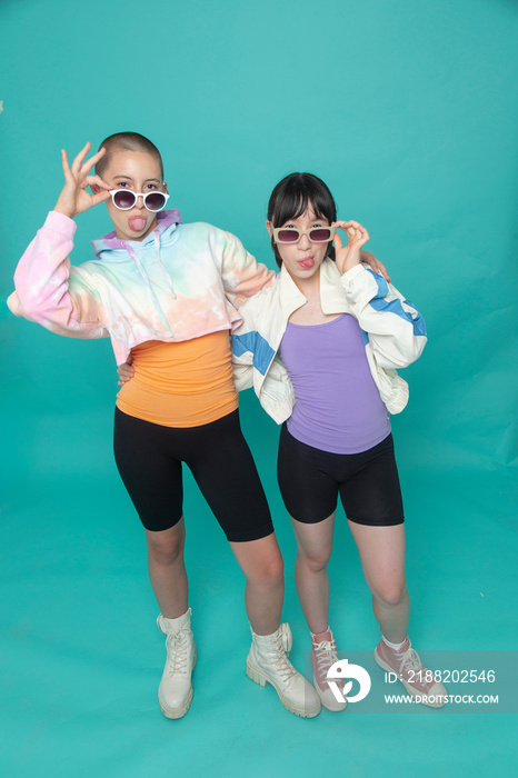 Studio portrait of two girls wearing sunglasses and sticking out tongues