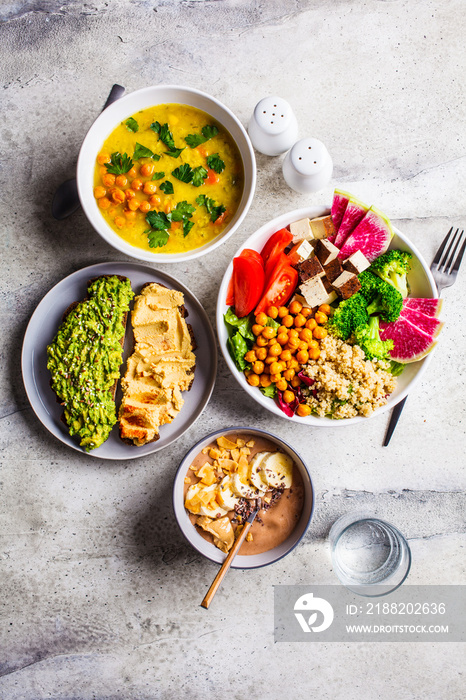 Flat lay of vegan food. Chocolate smoothie bowl, Buddha bowl with tofu, chickpeas and quinoa, lentil soup and toasts on a gray background.