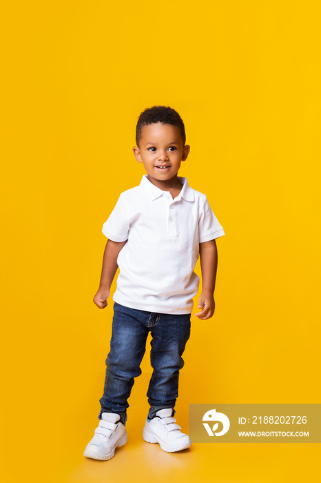 Cute little black boy standing in studio over yellow background