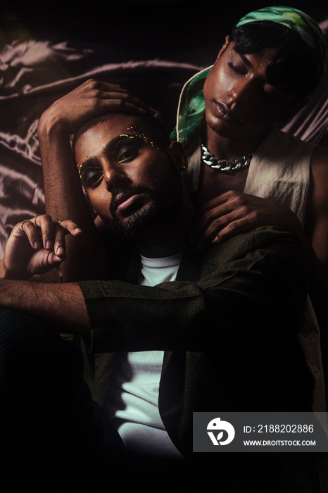 Two Malaysian Indian men in a studio setting with cloth flying in the background, posing against a black bacground