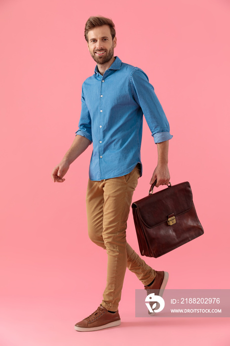 happy casual guy in denim shirt holding suitcase and smiling