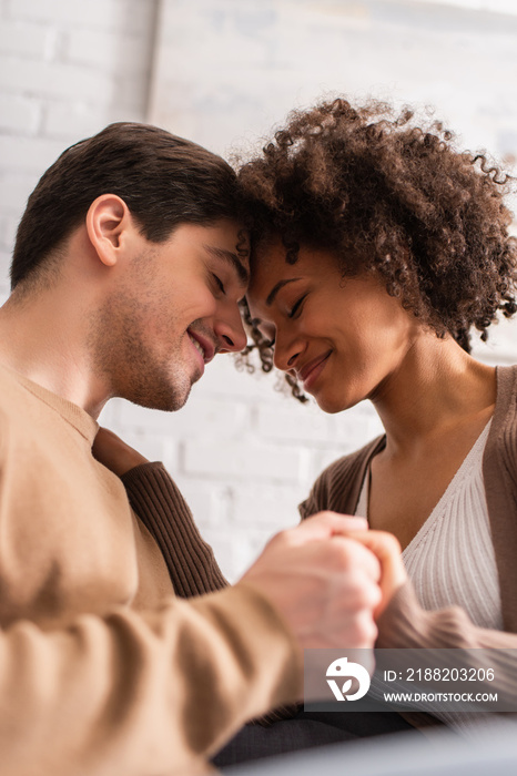 Multiethnic couple with closed eyes holding hands at home