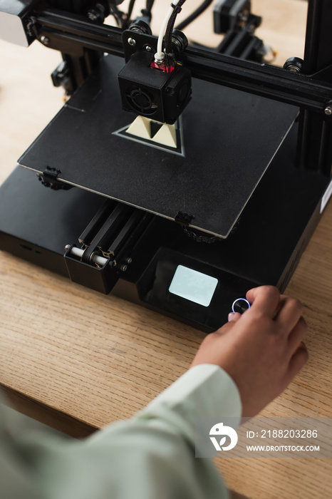 partial view of female hand touching button on 3D printer with produced model in office