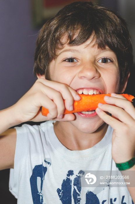 Happy little boy eating a fresh carrot and having fun.