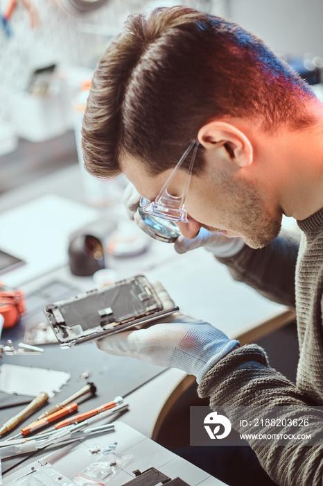 The technician uses a magnifying glass to carefully inspect the internal parts of the smartphone in a modern repair shop