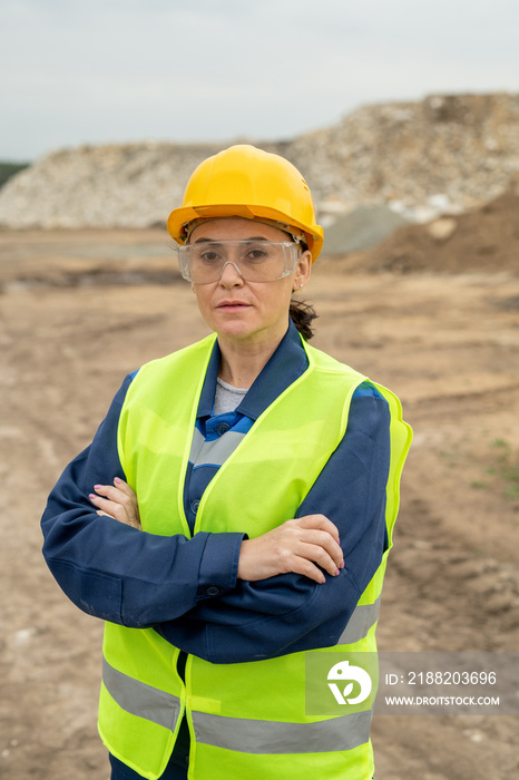 Female builder with crossed arms standing against quarry or construction site