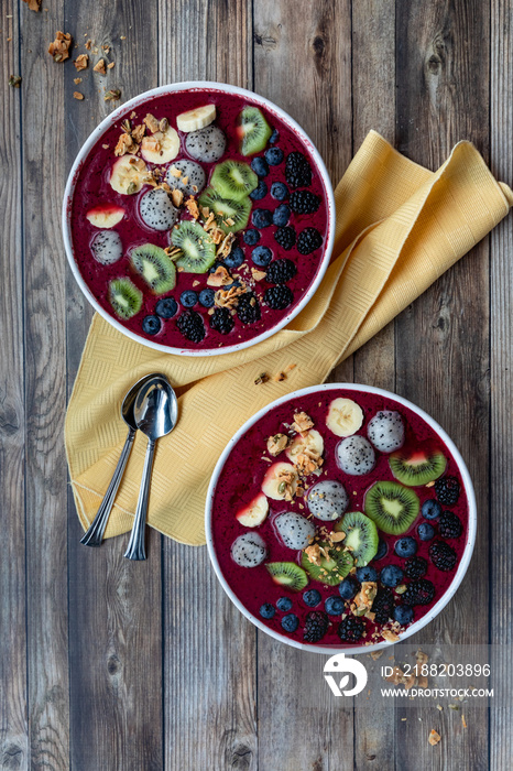 Top down view of acai berry bowls garnished with various sliced fruit and topped with granola.