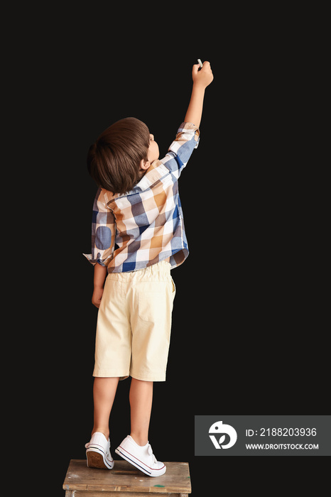 Cute little boy drawing with chalk on black wall