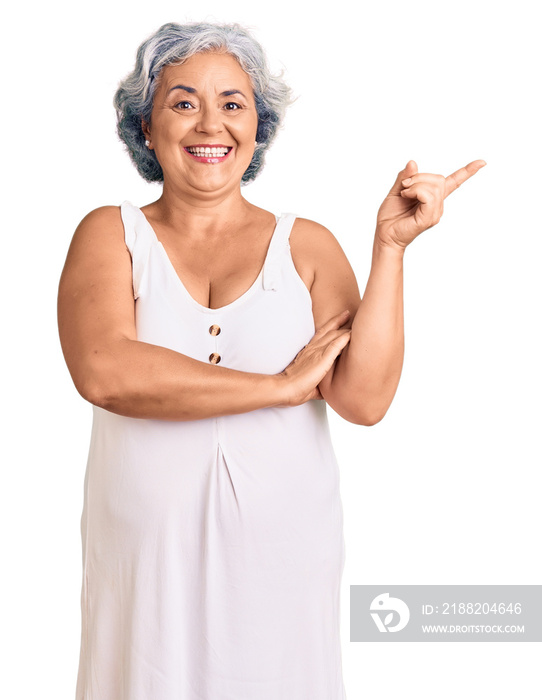 Senior woman with gray hair wearing casual clothes with a big smile on face, pointing with hand and finger to the side looking at the camera.