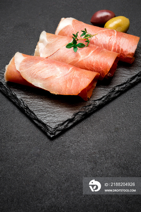 proscuitto ham arranged in thinly sliced rolls on stone serving board