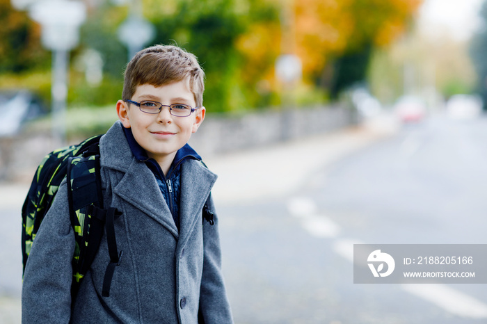 Happy kid boy with glasses and backpack or satchel. Schoolkid in stylish fashon coan on the way to middle or high school on cold autumn day. Healthy child outdoors on the street, on rainy day.