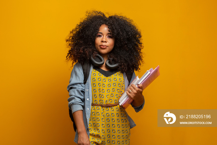 Female student in campus with books in her arms. Yellow background.