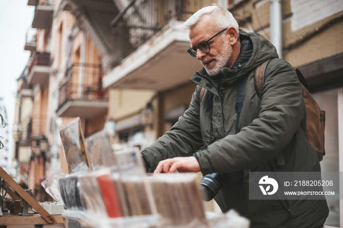 Senior man chooses vintage vinyl records at a flea market. Buys rare audio recordings, nostalgia.