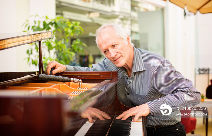 Elderly music instrument technician tuning a piano keyboard.