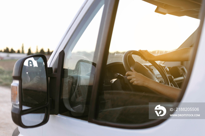 View from the outside of the steering wheel of a van and woman hands at sunset before starting the trip