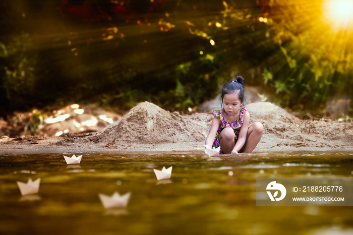 Cute asian little child girl playing paper boat in the riverside in summer time with fun and happiness