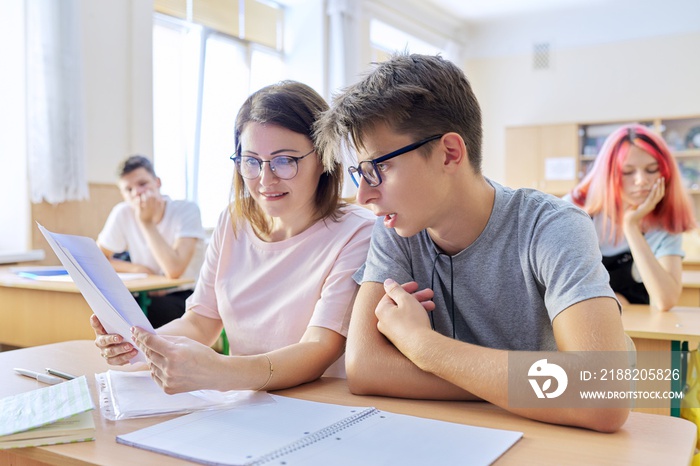 Middle-aged woman teacher sitting at desk with teenage student teaches