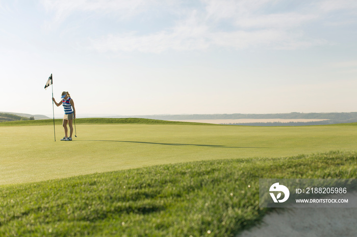 Mid-adult female golfer setting flag stick in hole