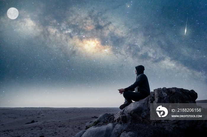 person sitting on the top of the mountain meditating or contemplating the starry night with Milky Way and Moon background in Atacama Desert