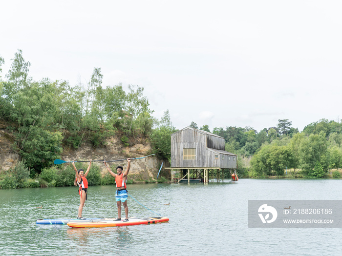 Friends standing with arms raised on paddleboards on lake