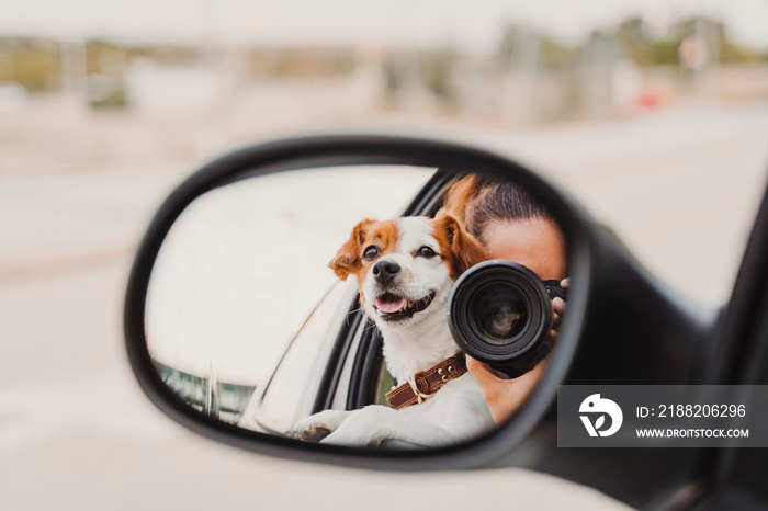 young woman taking a picture with camera on rear mirror of her cute small jack russell dog watching by the window. Ready to travel. Traveling with pets concept