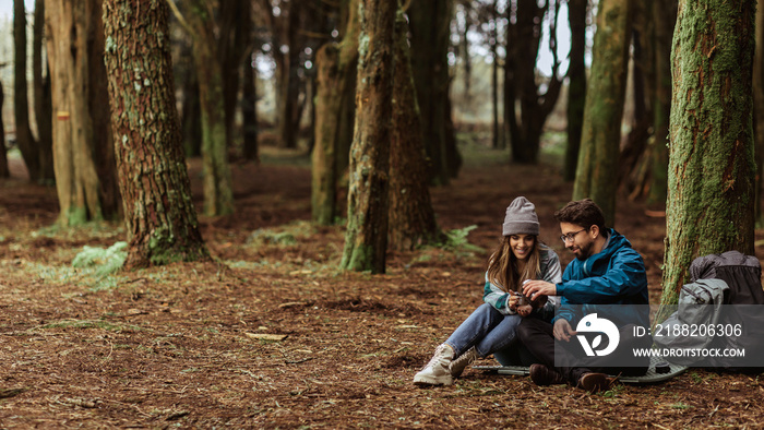 Smiling millennial caucasian couple in jackets with backpack travel in cold forest, enjoy adventure together outdoor