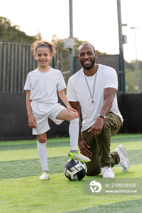 Portrait of man and girl (6-7) with ball on soccer field