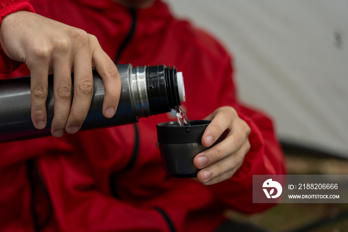 Young man drinking from insulated drink container while camping