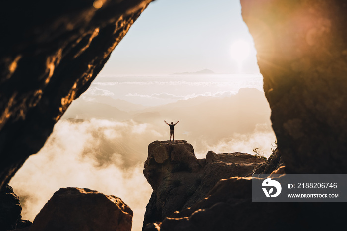 man on the top of a cliff during the sunset with raised hands