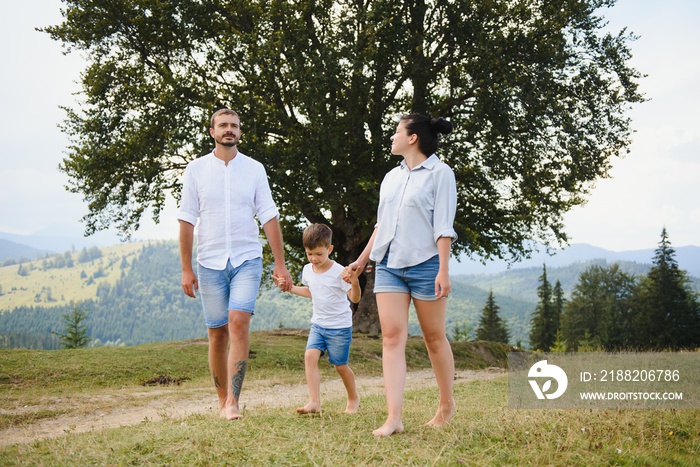 family walk on the field near the mountains in sunny day yellow grass father mother son holding hands on the sunset